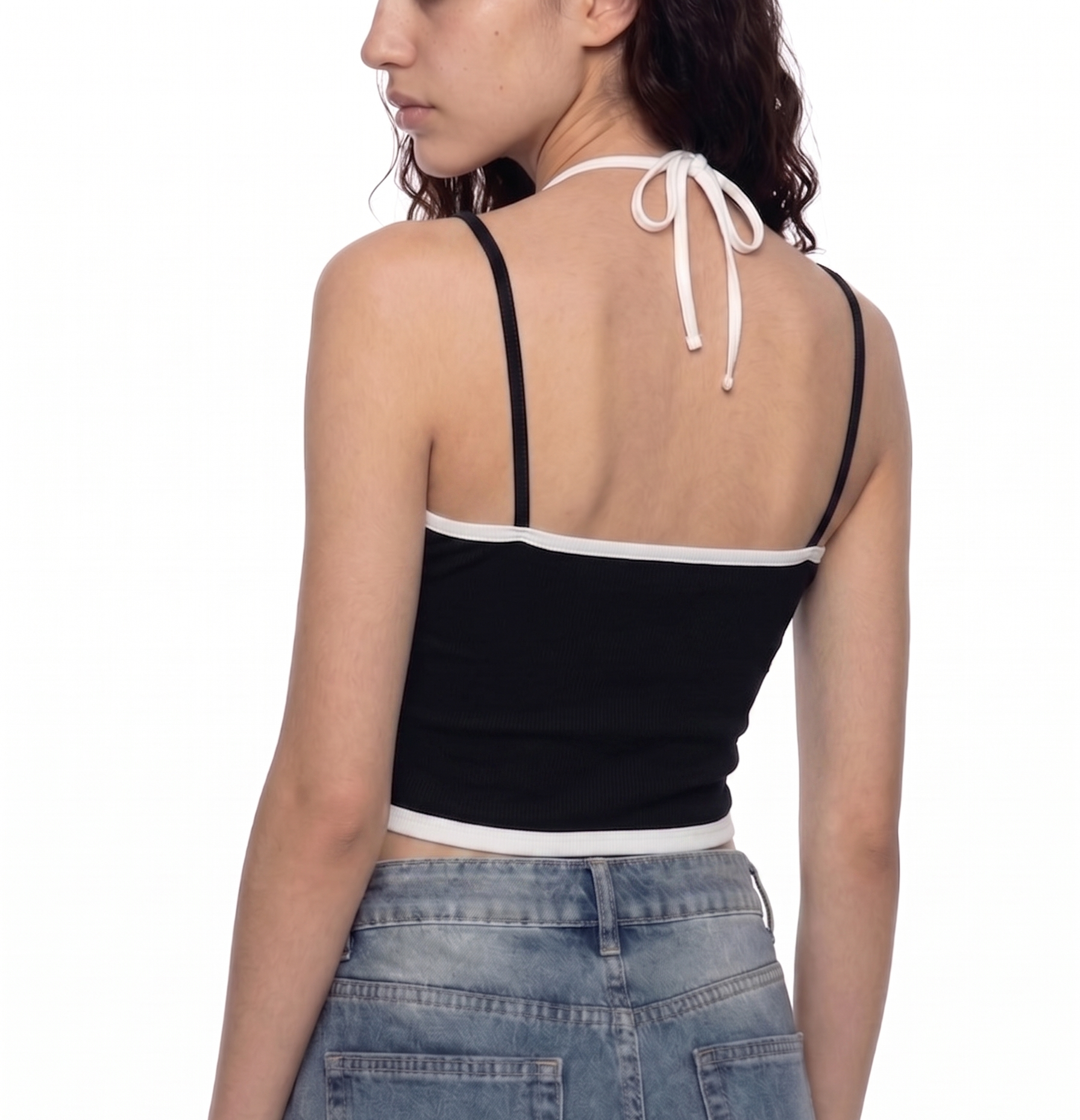 A woman shown from the back wearing a black crop top with white trim and thin shoulder straps that tie at the back, paired with light blue jeans, against a plain white background.