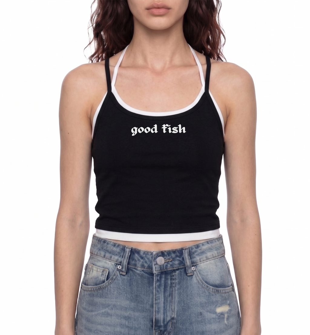 A model wearing a black ribbed halter crop top with white trim and the words 'good fish' printed in white gothic font on the chest, paired with light-wash blue jeans against a plain white background.